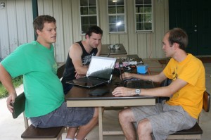 Jordan, Lincoln, and Brian sit outdoors and strategize how best to gather the Cherokee language data needed to understand the language's patterns.