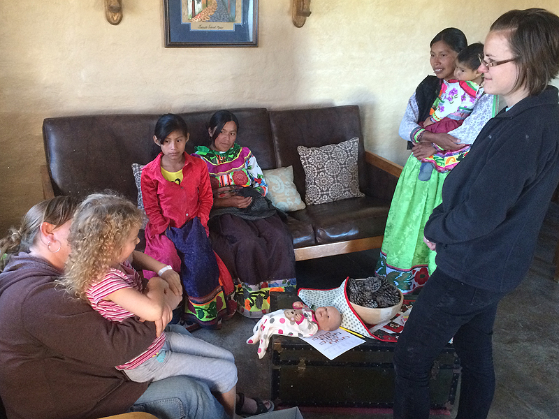 Amy and Elayne in a tribal house, visiting with Katie Moore and several Nahuatl ladies in colorful traditional clothing.