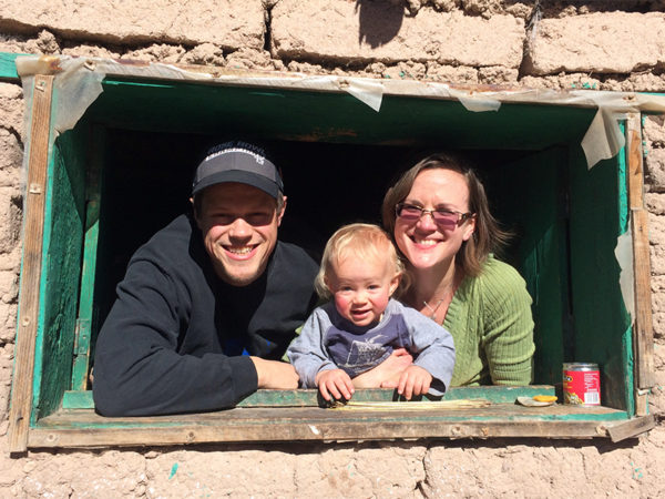Jordan, Joel and Amy smile out from a tribal house's window