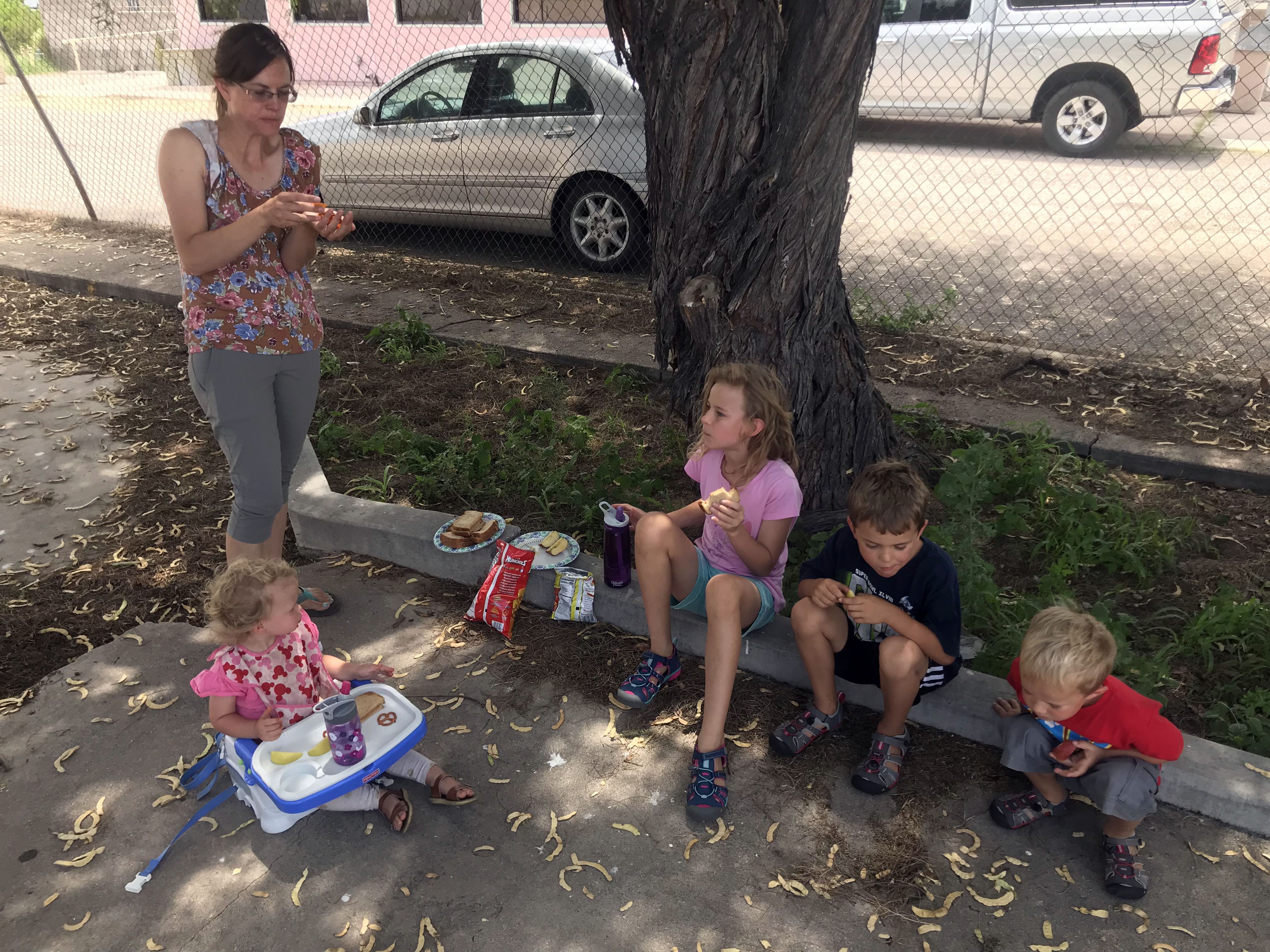 Lily, Amy, Elayne, Titus, and Joel eating curbside (quite literally), enjoying some PB&J at one of our midday stops while on the road!
